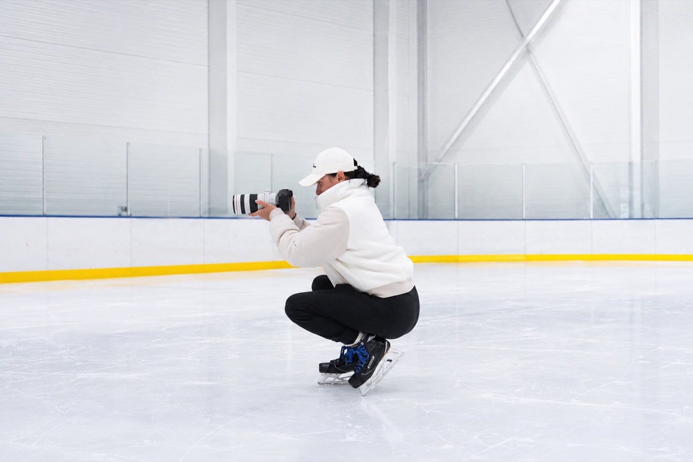 Fotografin kniet mit Kamera auf dem Eis und fotografiert in einer leeren Eishalle