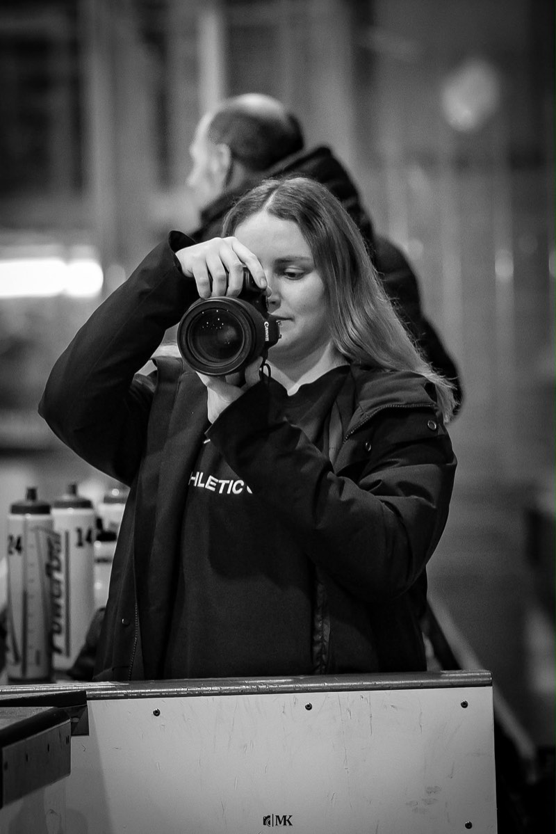 Fotografin mit Kamera am Spielfeldrand in der Eishalle, Schwarzweissbild