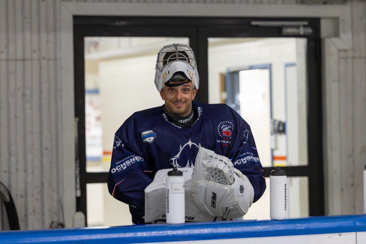 Gianluca lehnt mit hochgeschobener Goalie-Maske lachend an der Bande